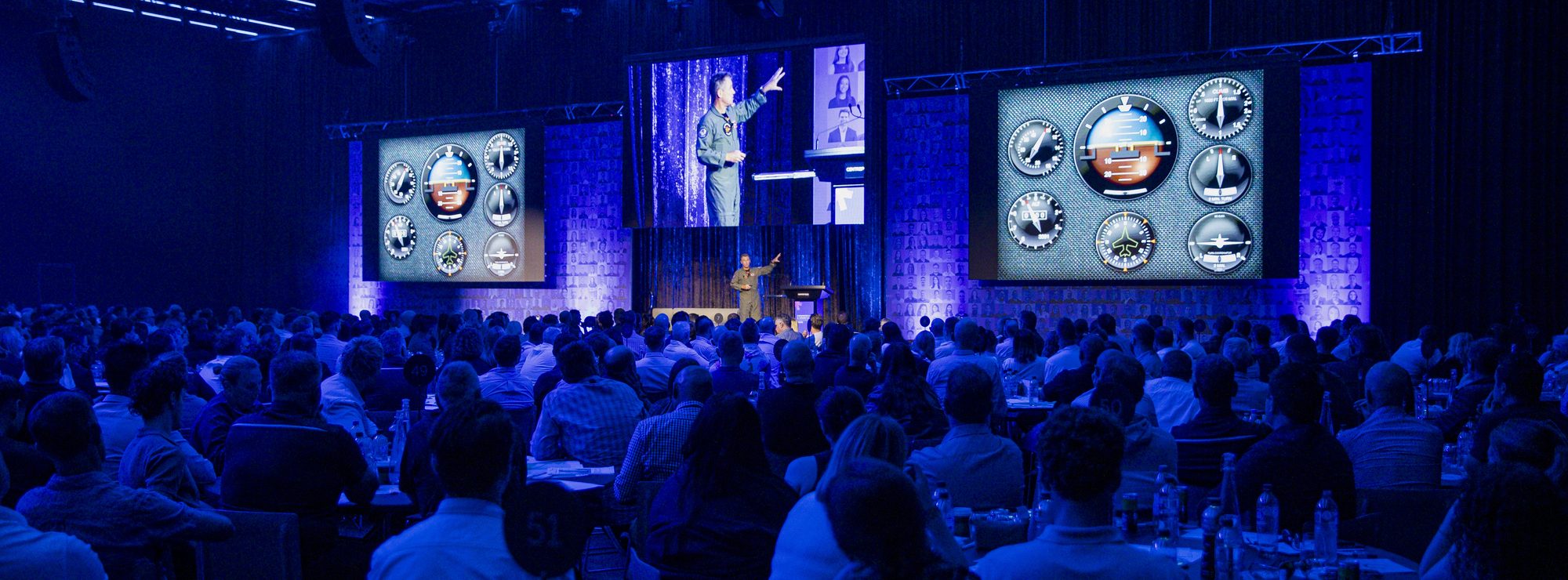 An Afterburner fighter pilot presenting on stage to a full conference room of seated delegates