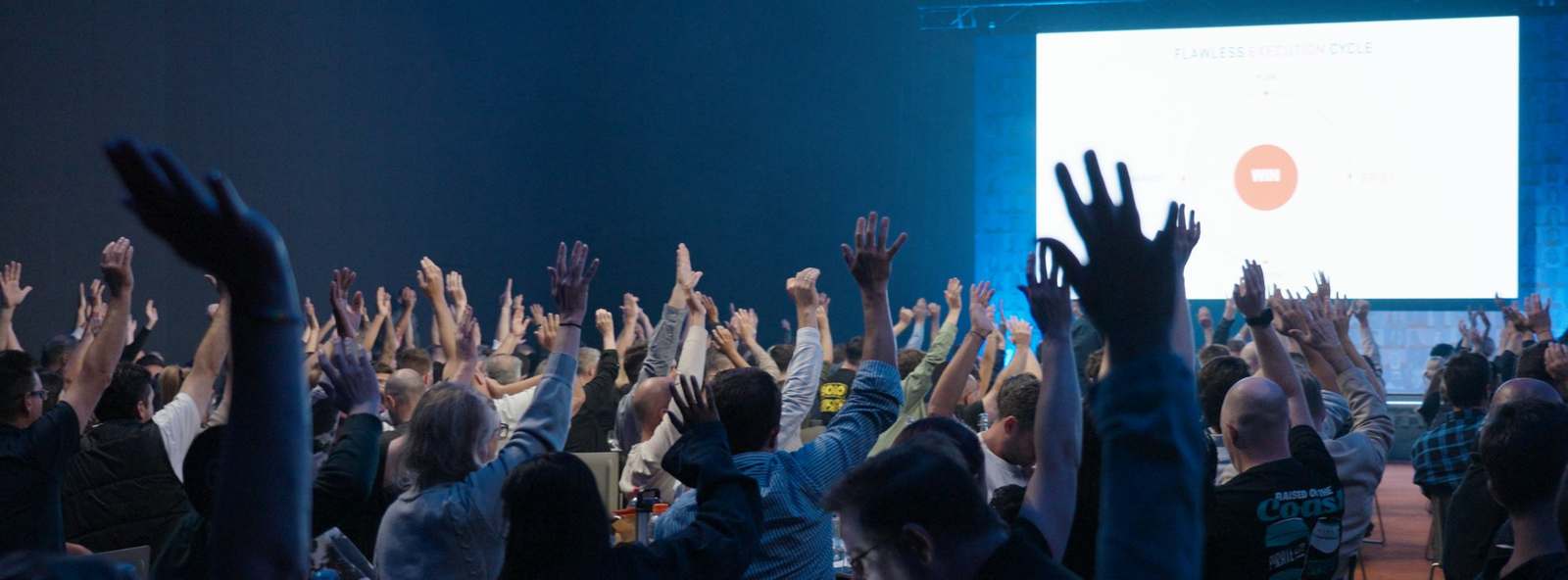 A conference room of delegates with their hands raised during an Afterburner session